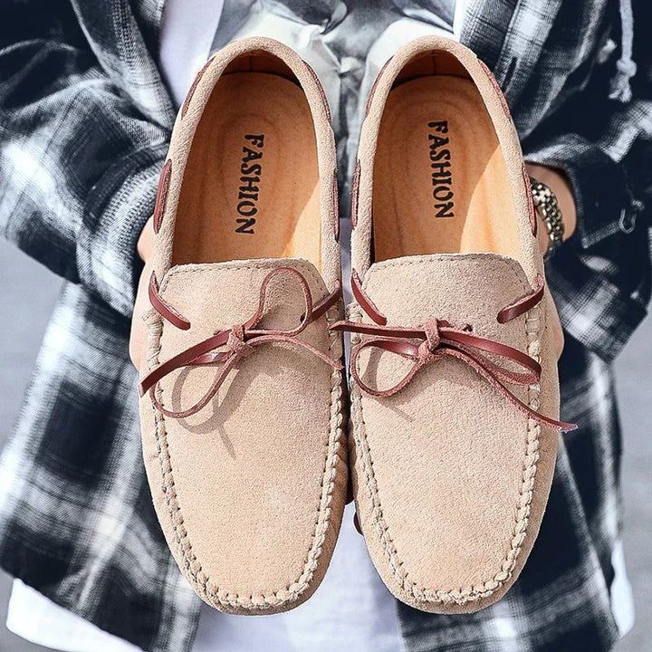 Pair of beige suede loafers with brown leather ties held by person in black plaid shirt