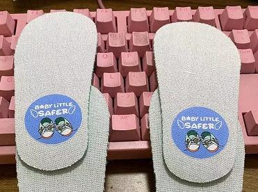 Pair of white baby shoe insoles with blue ‘Baby Little Safer’ labels on a pink keyboard