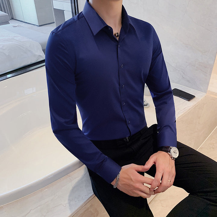 Man wearing a fitted navy blue dress shirt and black pants sitting on a marble bathtub edge