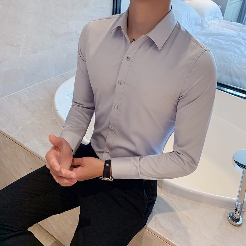 Man wearing light gray long-sleeve dress shirt and black pants sitting on marble edge beside bathtub
