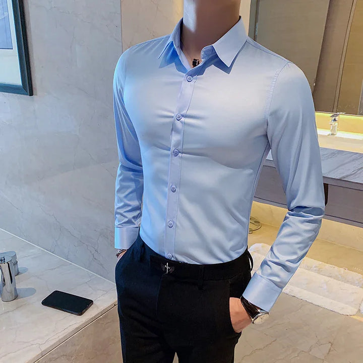Man wearing a fitted light blue dress shirt and black pants in a modern bathroom setting