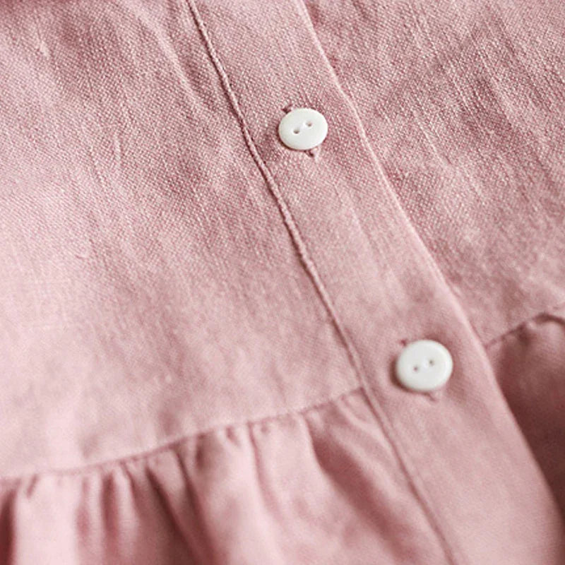 Close-up of pink linen fabric with white buttons and gathered seam detail on clothing