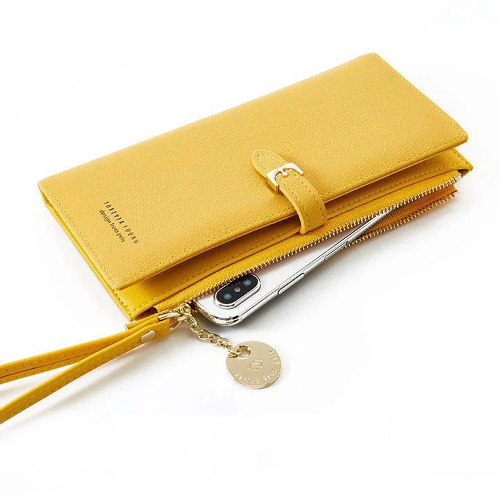 Yellow leather wallet clutch with buckle and zipper pocket holding smartphone, featuring wrist strap and gold charm