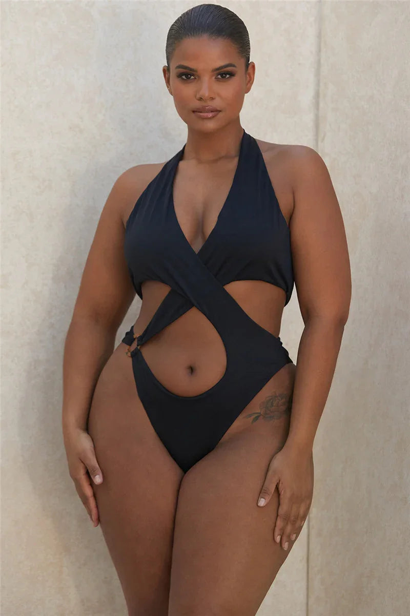 Plus size woman modeling black cut-out one-piece swimsuit against beige wall
