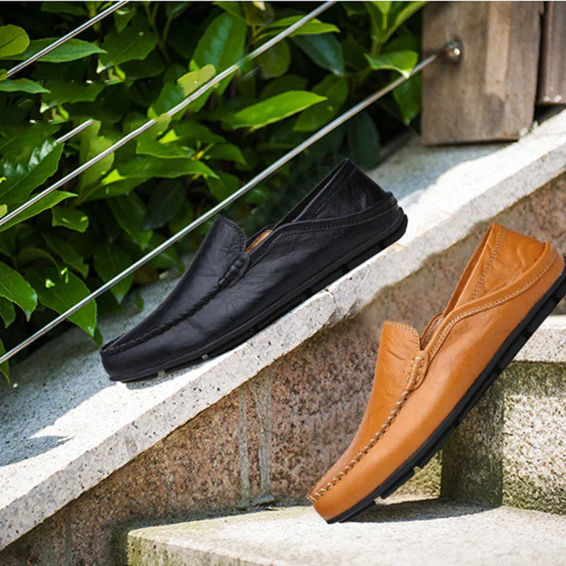 Black and brown leather casual loafers displayed on outdoor stone steps with green foliage background