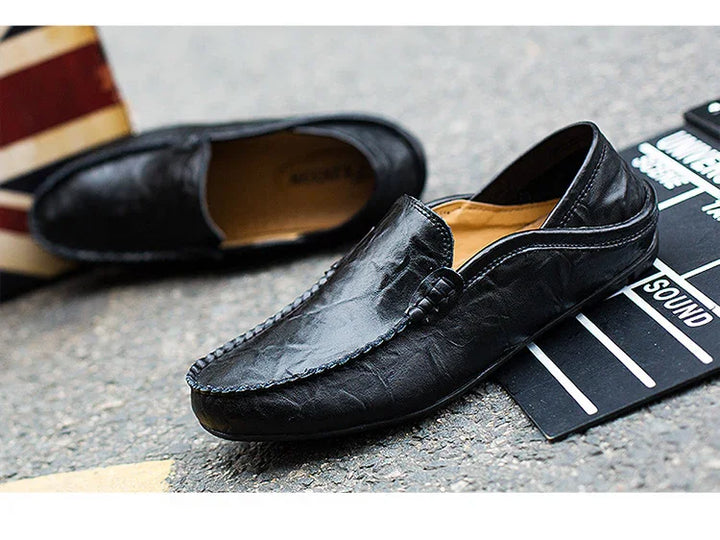 Black leather men's loafers on asphalt with striped box and film clapboard nearby