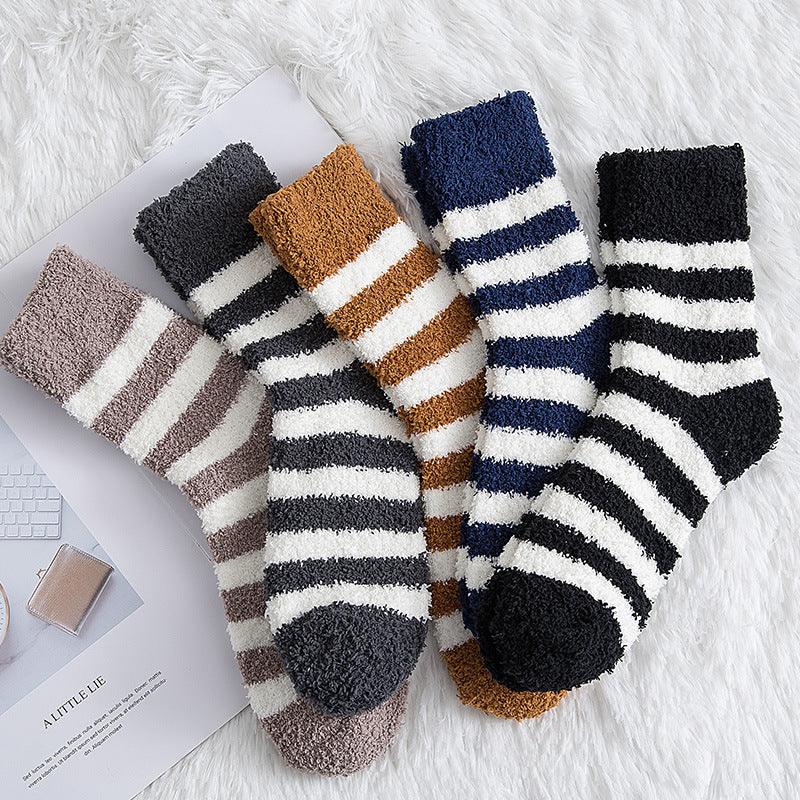 Five pairs of cozy striped fuzzy socks in beige, gray, brown, navy, and black on a white furry surface