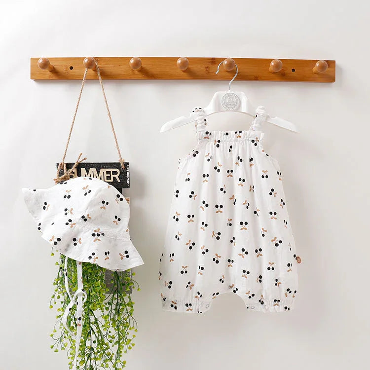 White baby romper and matching hat with black and beige floral pattern hanging on wooden peg rack