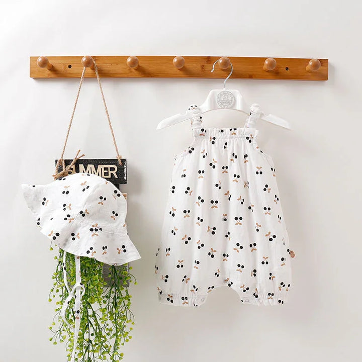 White baby romper and matching hat with black and beige floral pattern hanging on wooden peg rack