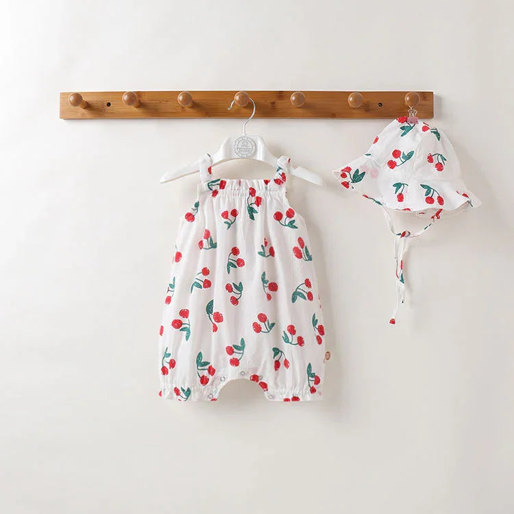 White baby romper and matching hat with red cherry print hanging on wooden rack