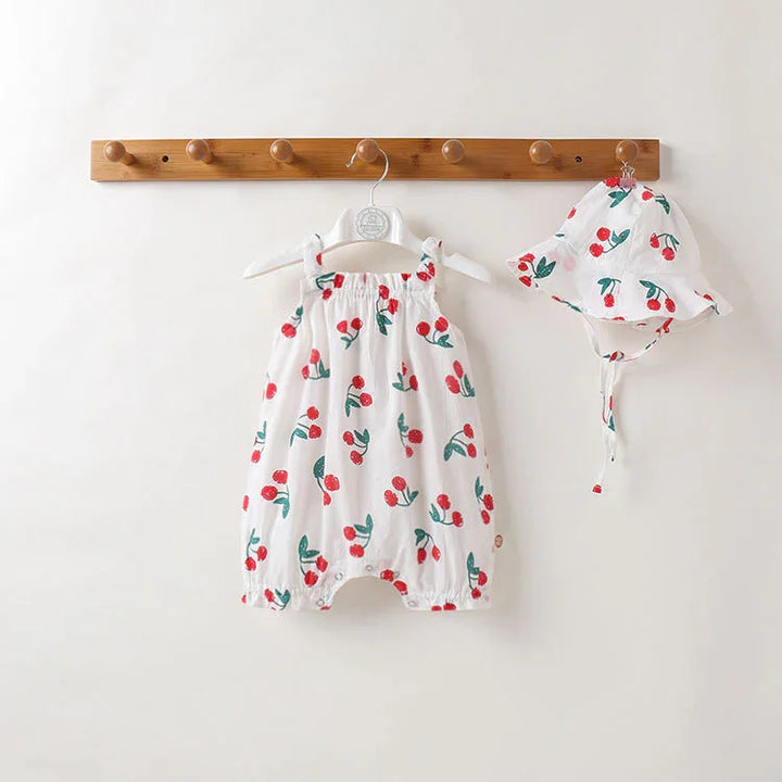 White baby romper and matching hat with red cherry print hanging on wooden rack