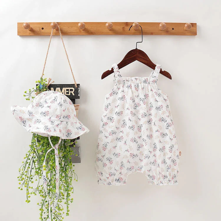 White floral baby romper and matching sun hat hanging on wooden hooks with green plant