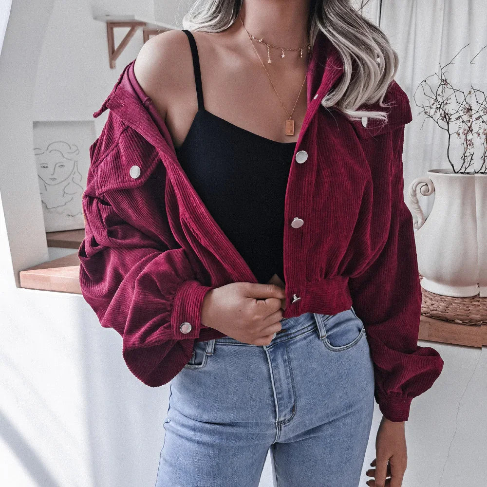 Woman wearing cropped burgundy corduroy jacket over black tank top and light blue high-waisted jeans
