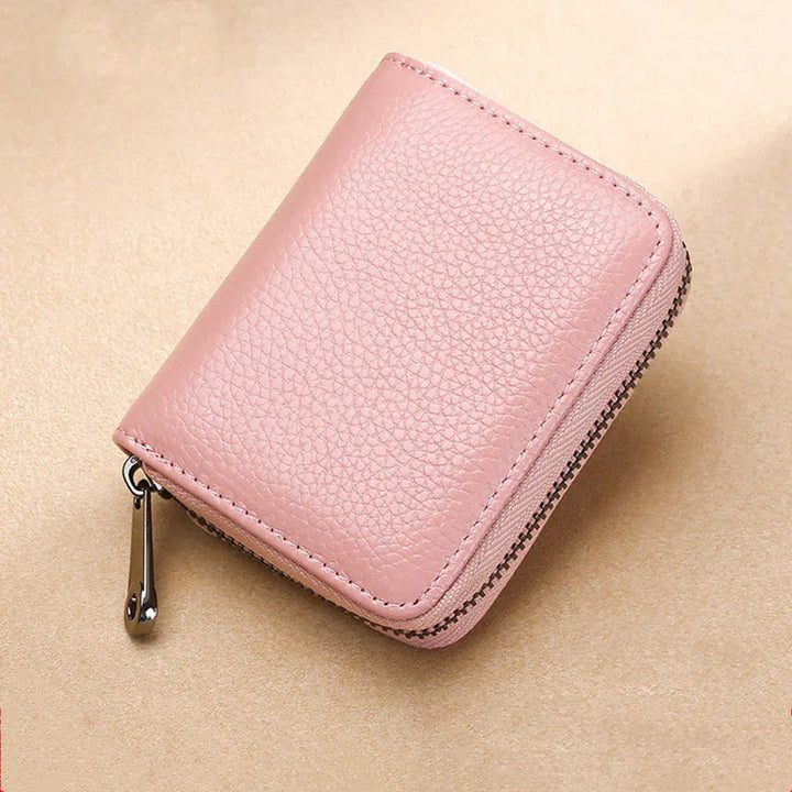 Small pink leather zippered wallet with textured surface on beige background