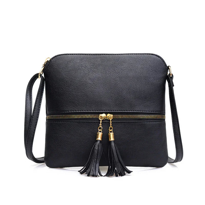 Black leather crossbody bag with gold zipper and tassel accents on white background