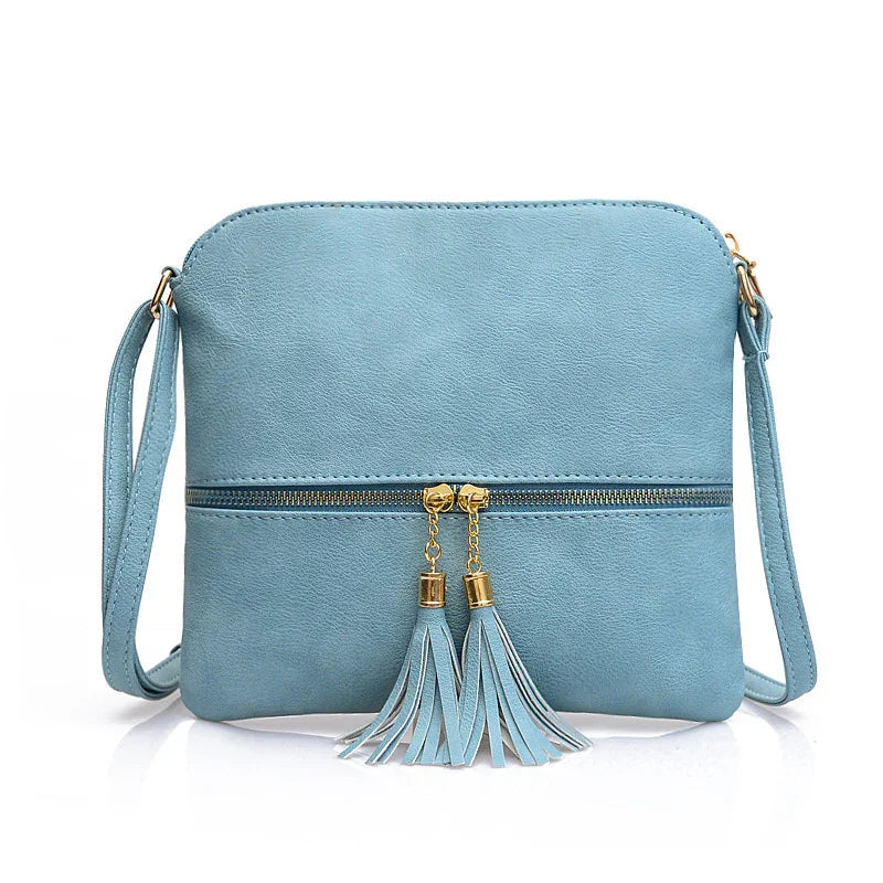 Light blue leather crossbody bag with gold zipper and tassel details on white background