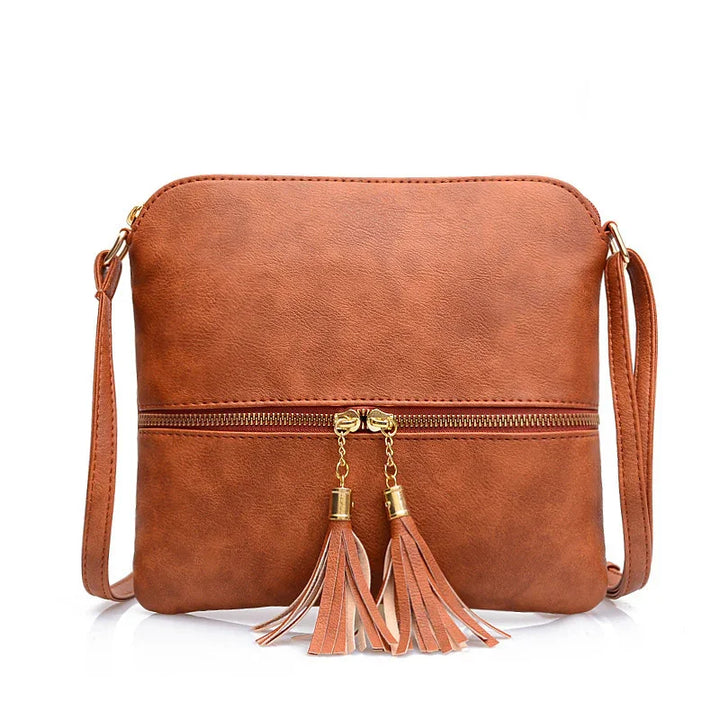 Brown leather crossbody bag with gold zipper and tassel details on white background