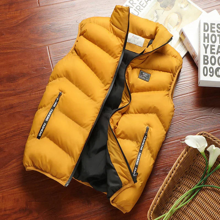 Mustard yellow puffer vest with black lining and zipper pockets on wooden surface with books and flowers