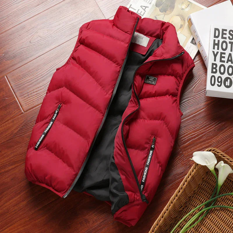 Red padded sleeveless winter vest with black zipper pockets, laid on wooden floor with books and white flowers