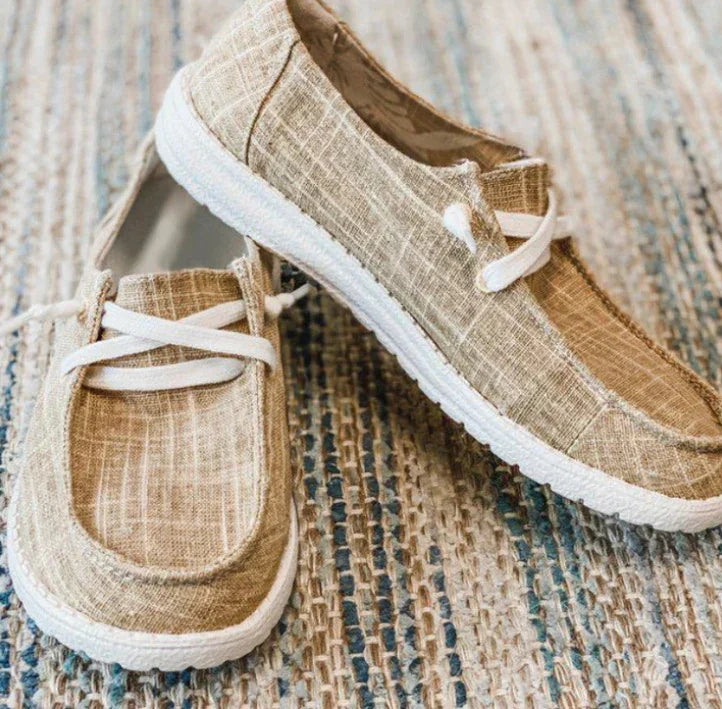 Light brown casual slip-on canvas shoes with white laces and textured rubber soles on woven rug
