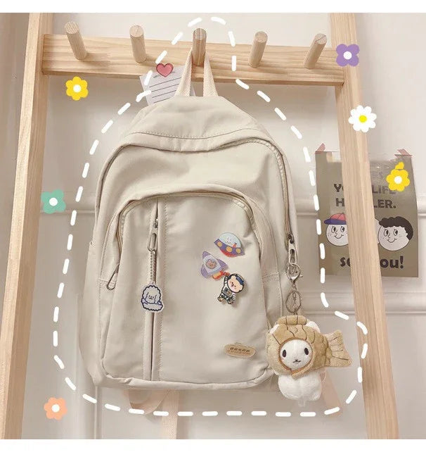 Cream backpack with cute character patches and plush keychain on wooden rack, kawaii style