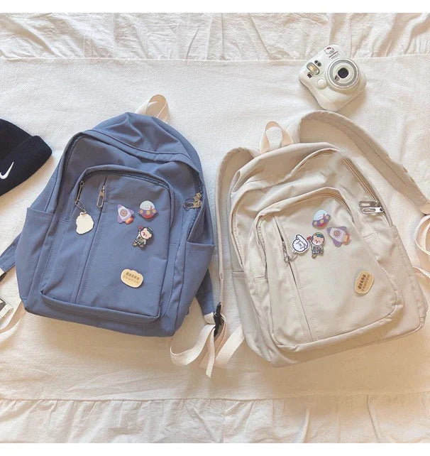 Blue and beige backpacks with cute pins on bed, instant camera nearby