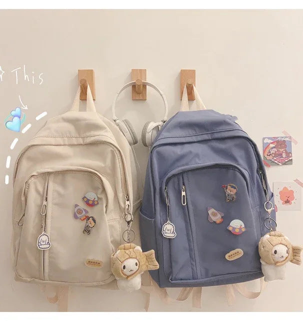 Cream and blue cute backpacks with plush keychains, cartoon pins, hanging on wooden hooks