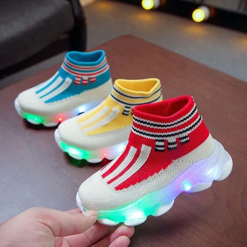 Three colorful toddler light-up sneakers in red, yellow, and blue on a wooden table