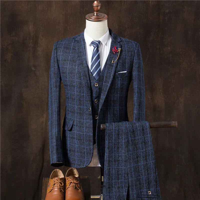 Men's blue checkered three-piece suit with striped tie, white shirt, red lapel pin, and brown leather shoes