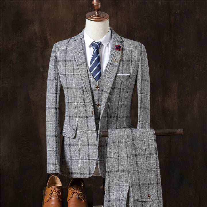 Gray plaid three-piece suit with white shirt, striped blue tie, flower lapel pin, and brown leather shoes