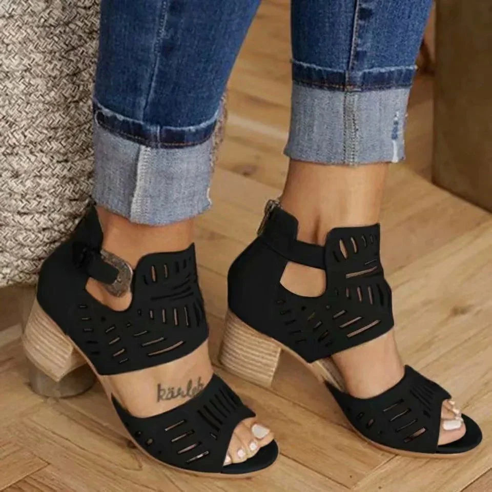 Black cutout open-toe block heel sandals worn with cuffed blue jeans on wooden floor