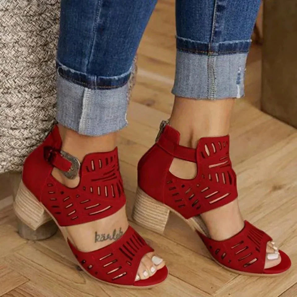 Close-up of feet wearing red cutout heeled sandals with ankle straps and cuffed blue jeans on wooden floor