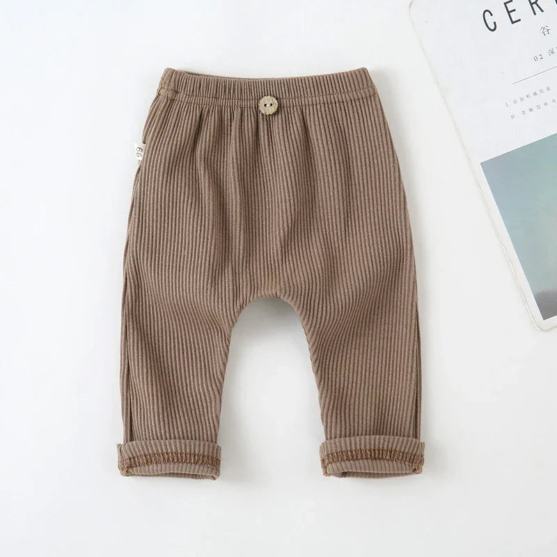 Brown ribbed baby pants with elastic waistband and wooden button detail on white background