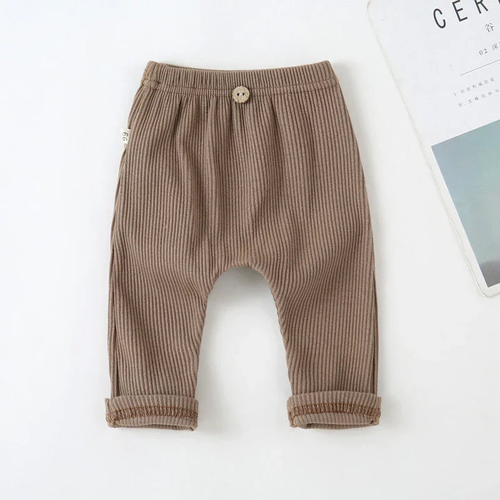 Brown ribbed baby pants with elastic waistband and wooden button detail on white background