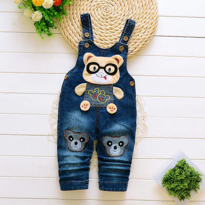 Cute baby denim overalls with teddy bear patches and glasses design on white wooden background