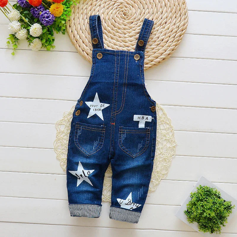 Dark blue denim baby overalls with white star patches and button straps on white wooden floor