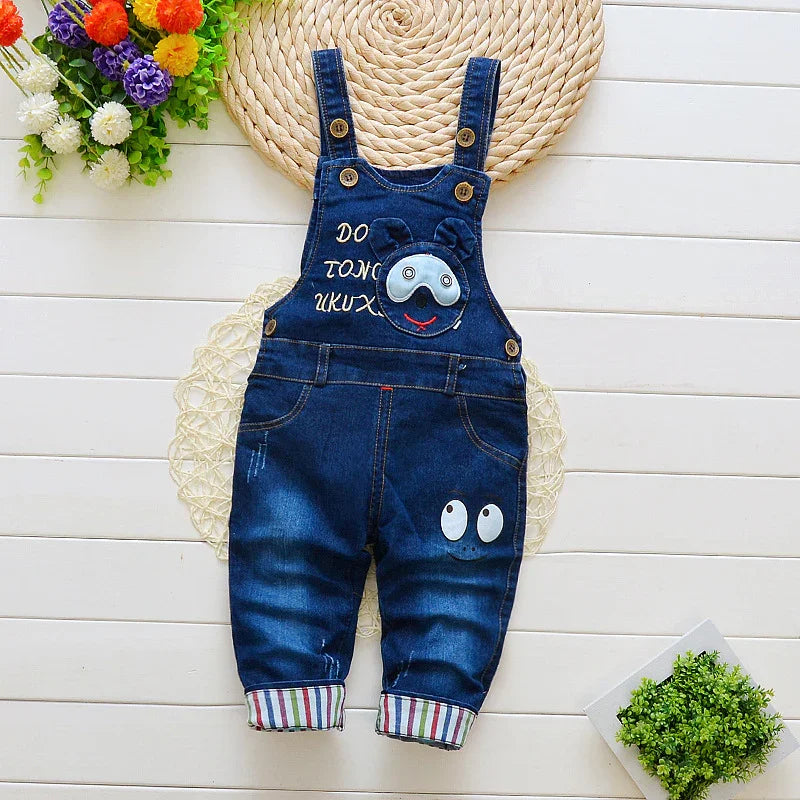 Blue denim baby overalls with cartoon bear face and eye designs, striped cuffs, and button straps
