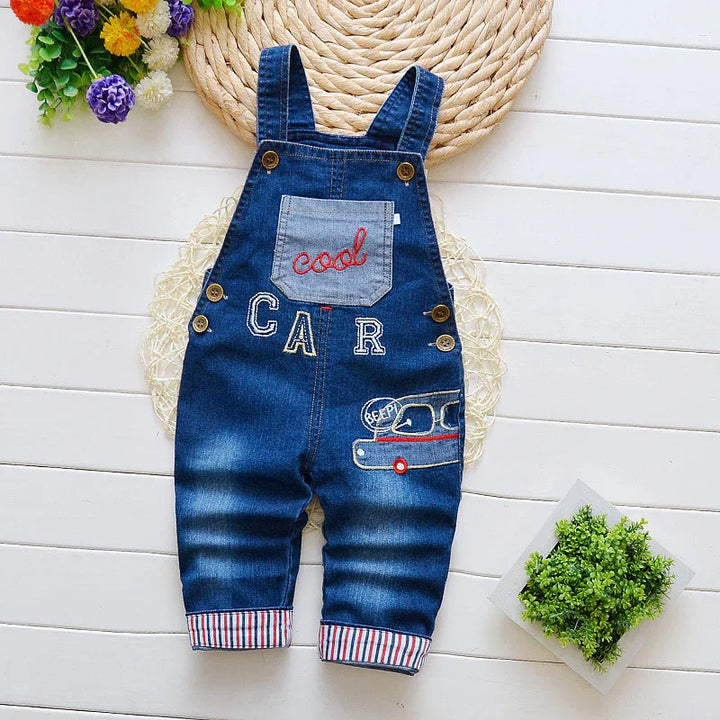 Toddler denim overalls with car embroidery and cool patch on white wooden floor