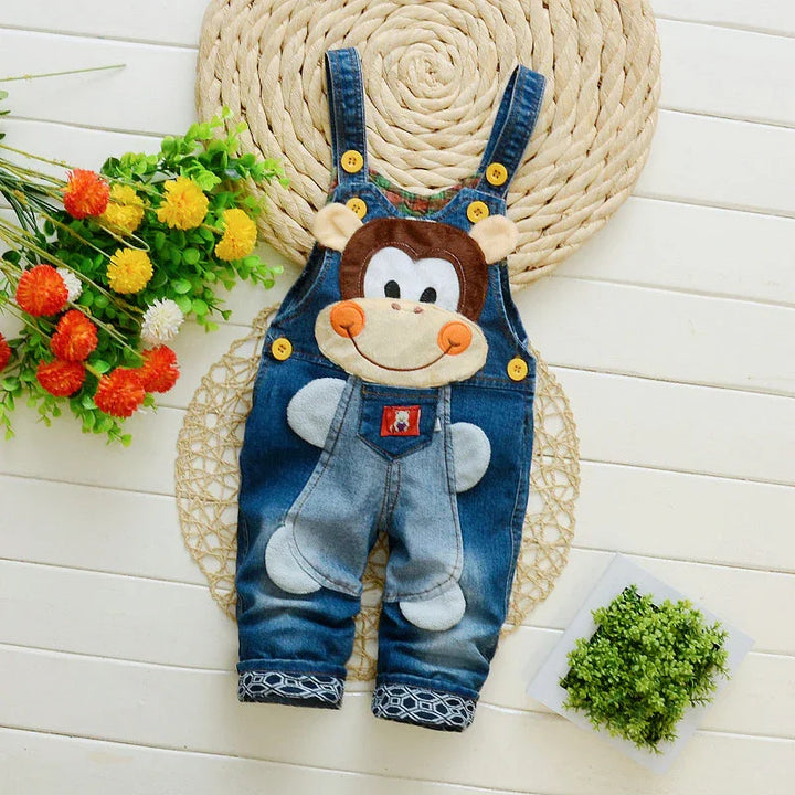 Cute baby denim overalls with smiling monkey face applique, yellow buttons, and patterned cuffs on woven mat