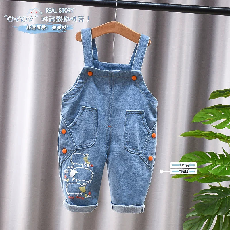 Blue denim baby overalls with orange buttons and sheep embroidery hanging on wooden hanger