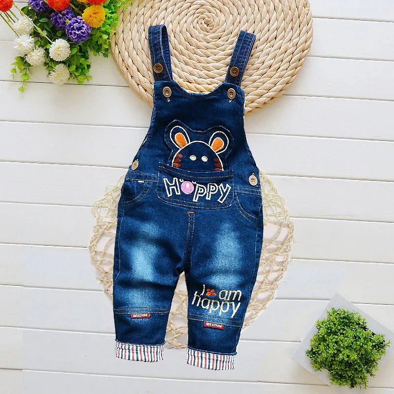 Blue denim baby overalls with cartoon bear and 'Hoppy' and 'I am happy' embroidery on white wooden background