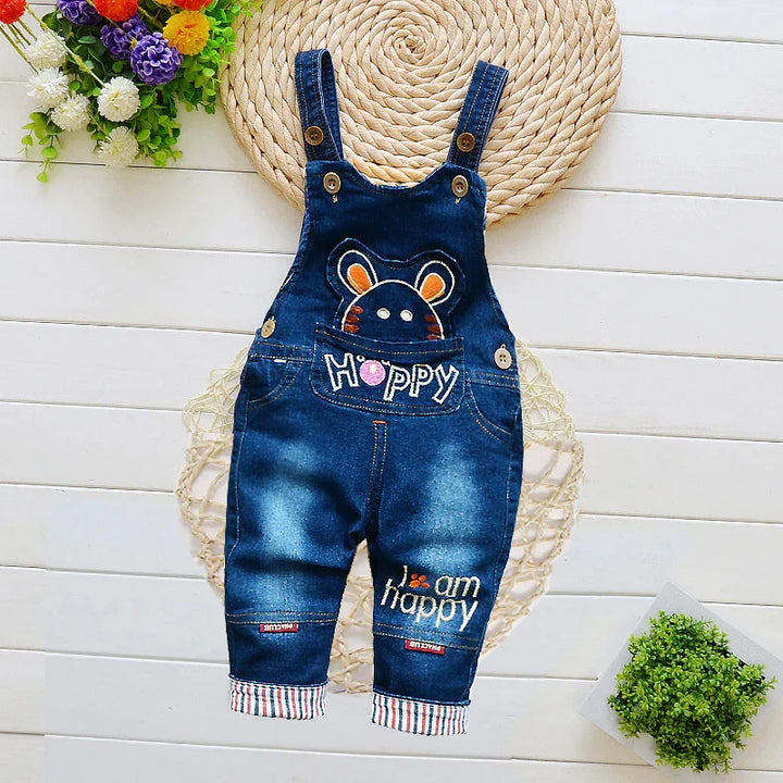 Blue denim baby overalls with cartoon bear and 'Hoppy' and 'I am happy' embroidery on white wooden background