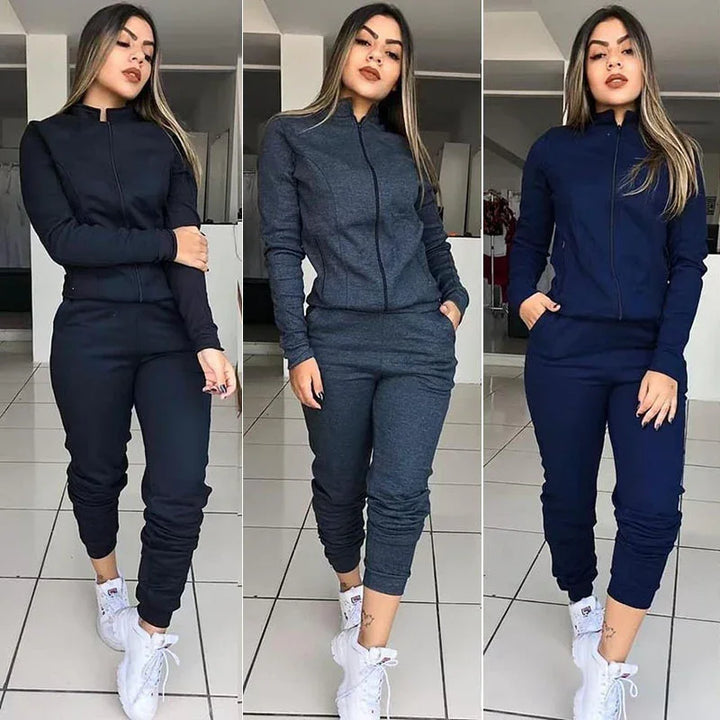 Woman modeling black, dark gray, and navy blue zip-up tracksuits with white sneakers indoors