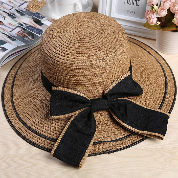 Stylish brown woven sun hat with a wide brim and a black bow on a wooden surface
