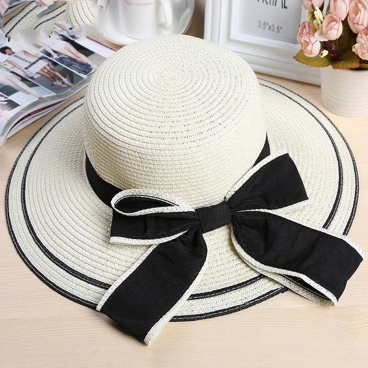 Stylish white woven sun hat with wide brim and black ribbon bow on wooden table