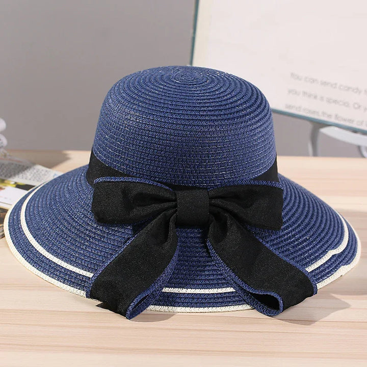 Blue woven sun hat with wide brim, white trim, and large black bow detail on wooden surface