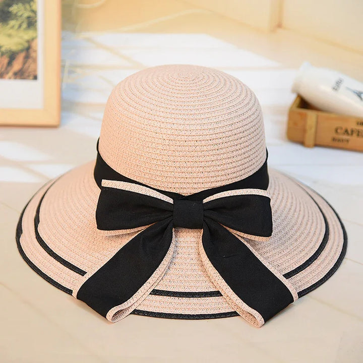 Beige wide-brim sun hat with black ribbon bow and trim on a light surface