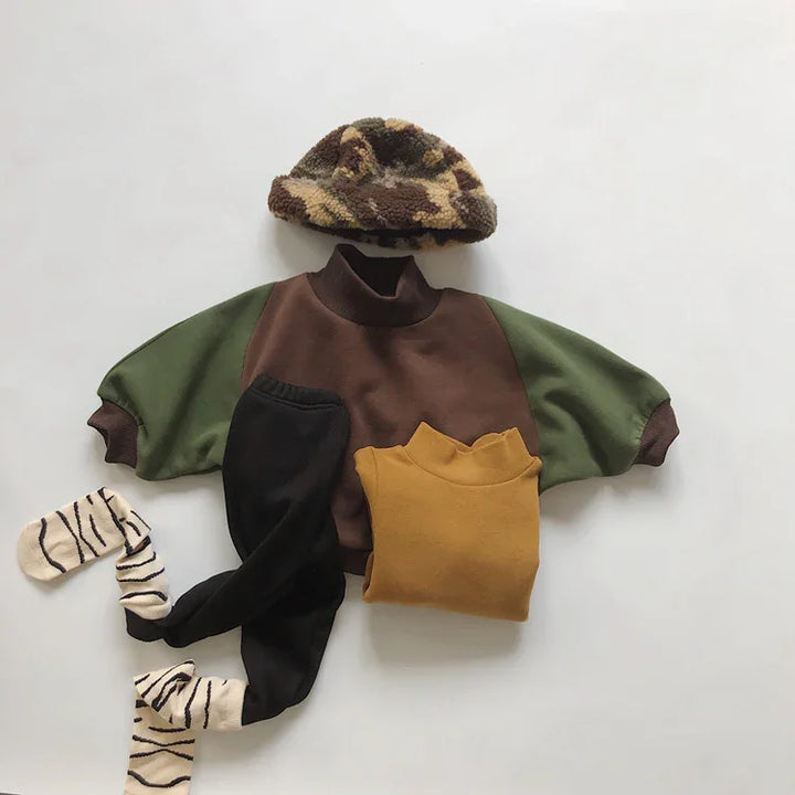 Kids outfit with green and brown sweatshirt, black pants with striped socks, mustard top, and camo bucket hat