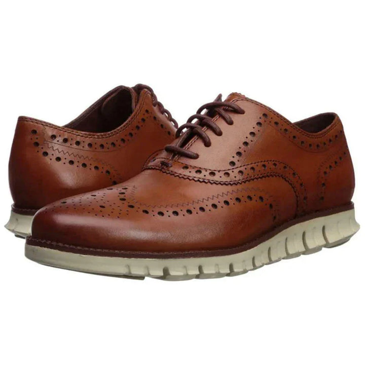 Brown leather brogue wingtip shoes with white rubber sole and decorative perforations
