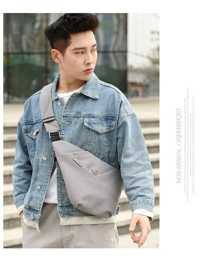 Young man wearing a blue denim jacket and gray crossbody bag outdoors on urban steps